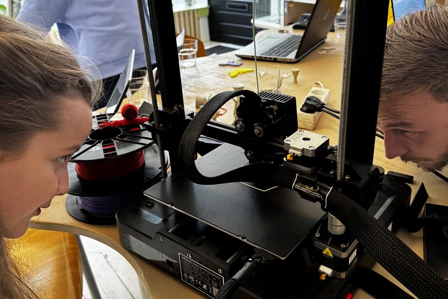 Een geel geprint kattenkopje staat op de plaat van een 3D-printer.