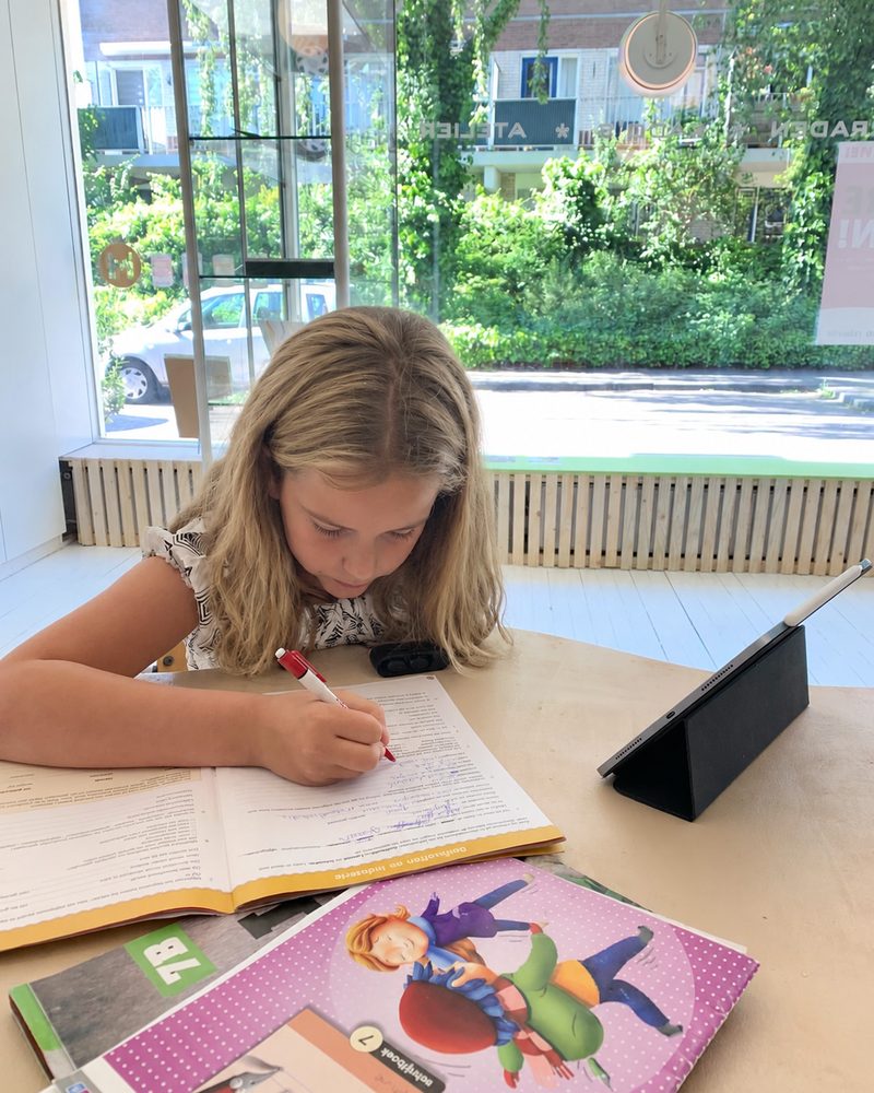 Een meisje maakt sommen in een werkboek aan de werktafel bij JJED-Educatie.
