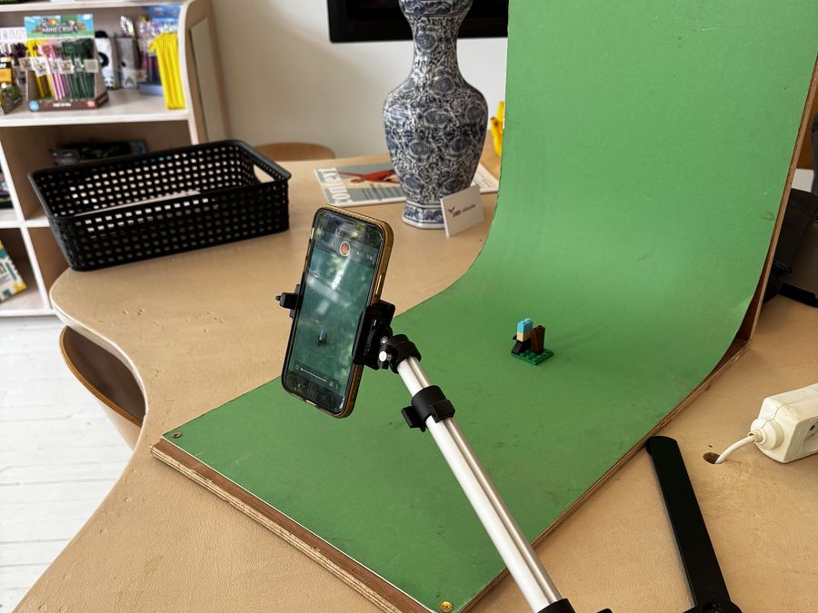 Een opstelling voor stop motion: een telefoon op statief gericht op een klein figuurtje voor een groen doek.