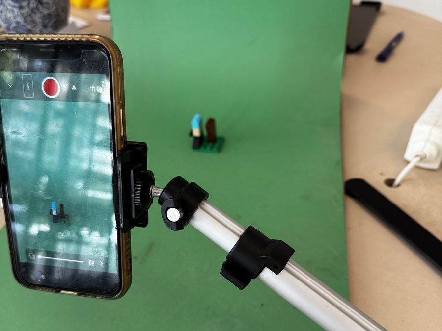 Een telefoon op een statief filmt een klein Lego-figuurtje voor een groen doek.