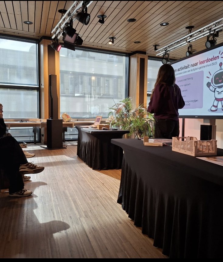 Evelien geeft de workshop Programmeren zonder scherm in Rozet; op het scherm staat een dia over leerdoelen voor digitale geletterdheid.